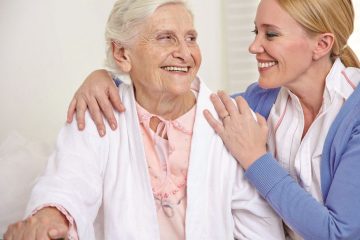 Lächelnde Frau umarmt eine glückliche Seniorin im Seniorenheim Lächelnde Frau umarmt eine glückliche Seniorin im Seniorenheim